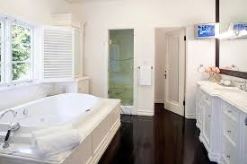 Rustic wood floors provide a dose of warmth in the otherwise white bathroom. Wainscoted Tub With Marble Deck Under Shuttered Windows Transitional Bathroom