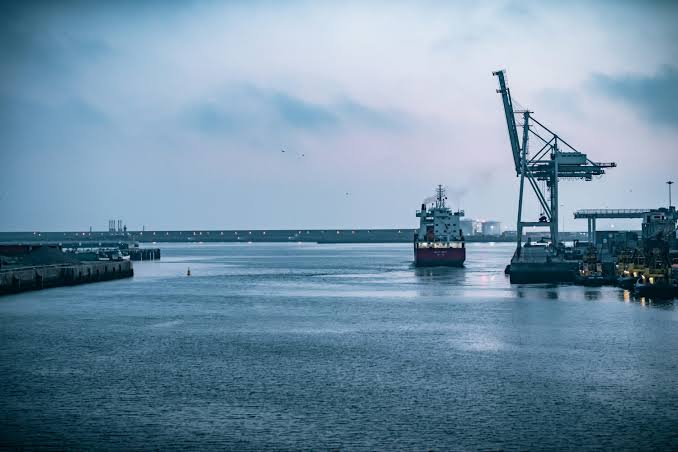 Commercial grain ships docked at a Black Sea port with silos visible in the background under an overcast sky.