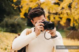 In return for a fee, the client can use the pictures in their book or on their website. Handsome Young Photographer Standing In Autumn Park And Taking Photo With Camera Trip Hairstyle Stock Photo 293868518