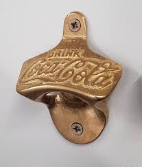 It's wall mounted, made of stainless steel and you can pick one up from drinkstuff.com for £19.95 by clicking here. Wall Mounted Coca Cola Bottle Opener Cargo Plus