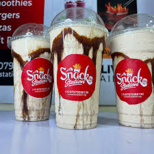 A tall glass of banana smoothie with a straw and mango slices on a white background