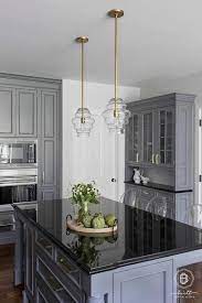 Grey kitchen cabinets with black quartz countertops. Gray Kitchen Island Featuring A Black Quartz Countertop Under A Set Of Mini Glass And Brass Lanter Black Kitchen Countertops Grey Kitchen Kitchen Black Counter