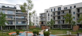 Studierende und als gäste forschende sitzen in einer begrünten und mit vereinzelten laubbäumen bewachsenen atriumanlage und genießen gemeinsam in regem austausch einen lauen sommerabend. Abg Quartier Mitte Riedberg Frankfurt