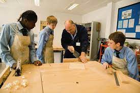 Woodwork Teacher Showing Students How To Saw Wood - Stock Image - C046/7469  - Science Photo Library