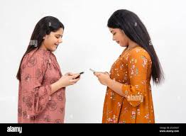 Two young teenager Indian girls busy on their smart phones, standing  against white studio backdrop Stock Photo - Alamy