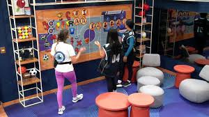 Três mulheres em uma sala com um painel de jogo temático de esportes, possivelmente em um reality show.