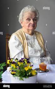 Alte grau behaarte Frau am Tisch sitzend mit Blumen und einer Tasse Kaffee  Stockfotografie - Alamy