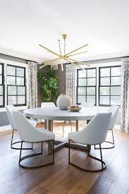 White And Gold Dining Chairs Surround A Round Concrete And Wood Dining Table Illuminated By A In 2020 Round Dining Room Table Gold Dining Chairs Concrete Dining Table