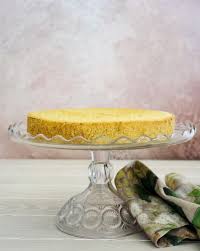 Large white transitional kitchen features a white center island with white ornate end panel trim illuminated by white and gold goodman hanging lamps and light wooden floors. Sponge Cake The Lemon Apron