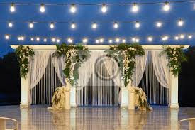 A few popular options include pomanders (small spheres of flowers that hang from loops or ribbon at the top), tying flowers onto chairs with fabric sashes, and filling jars with fresh blooms. Night Wedding Ceremony With Arch Orchid Flowers Palm Leaves Wandsticker Floral Torbogen Blumengeschaft Myloview De