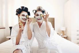 Sonriente madre y su hija con la belleza de la cara pack sentado en la cama  la celebración de rodajas de pepino a los ojos. mujeres felices relajarse  en la cama con