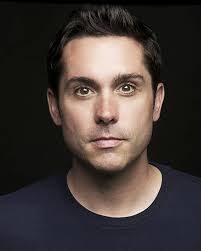 TIL Joseph May (US Player Voice) is a British born Canadian actor, who has  portrayed Edward Shames(Band Of Brothers), Doctor Blue(Resident Evil), Andy  Button in the TV series Episodes, The radio DJ