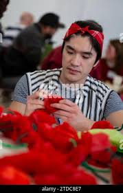 Seattle, Washington, USA. 17th December, 2023. Nick Woo (left) helps  attendees assemble paper flowers at a Portraits for Palestine event at the  Rainier Arts Cente. Jewish Voice for Peace organized the event