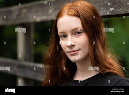 Ragazza di dodici anni dai capelli rossi con freckles in posa una  recinzione di sfondo di legno usurata Foto stock