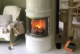 A corner wood burner fireplace, with a mantelpiece above, creates space for ornaments. Fireplace Insert Ronda 67 Camina Schmid