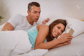Wife Cheating Her Husband Using Mobile Phone In Bed, Husband Is Catching  Her. Stock Photo, Picture and Royalty Free Image. Image 103516961.
