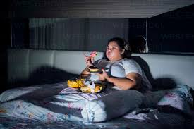 Fat Woman Eating Food On Bed At Home Stock Photo