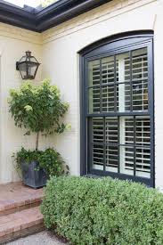An old fashioned, rustic style black front door on this red brick home is framed in concrete tones, with a simple arched transom window overhead. Midcentury Modern White Home Exterior With Black Windows Brick Exterior House Shutters Exterior Window Trim Exterior