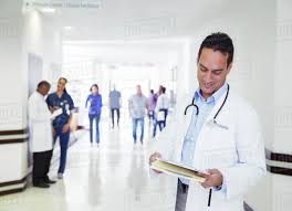 Doctor Reading Medical Chart In Hospital Hallway Stock Photo