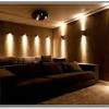 Custom media room home theater complete with gray sectional couch, gray carpet, black walls, projection tv, stainless steel wall sconces, and orange artwork to finish the look. 3