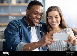 Happy Interracial Couple Watching Video Content On Smartphone While  Relaxing At Home Stock Photo - Alamy