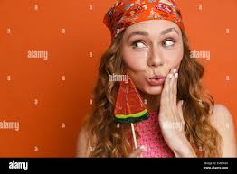 Young ginger woman expressing surprise while posing with lollipop isolated  over orange wall Stock Photo - Alamy