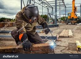 A Young Man Welder In Brown Uniform Welding Mask And Welders Leathers Weld Metal With A Arc Welding Machine At The Arc Welding Machine Arc Welding Welding