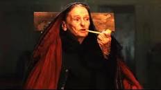 An old woman with a skull-like face smoking a pipe and with a shawl like that worn by a banshee