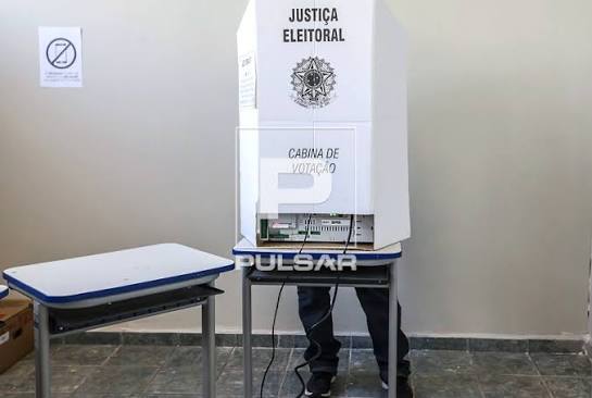 Eleitor votando em urna eletr&ocirc;nica nas elei&ccedil;&otilde;es majorit&aacute;rias 2018 - cartaz de proibido uso de celular na cabine de vota&ccedil;&atilde;o | Pulsar Imagens | Banco imagens do Brasil