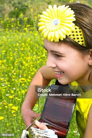 Cute Girl Playing Guitar To Daisy Field Stock Photo