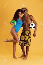 Young Beautiful Smiling Couple Holding Football And Volleyball Balls. Black  Man And European Woman Wear Beach Clothes. Concept Of Summer Beach  Vacation. Isolated On Yellow Background. Studio Shoot Stock Photo, Picture  and