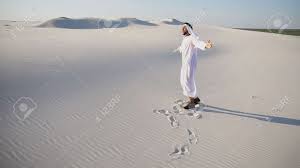 Handsome Arabian UAE Sheikh Man Dances On Spot And Drives Feet Along Soft  White Sand In Middle Of Bottomless Desert. Guy Sheikh Smiles And Laughs,  Rejoices And Jumps In National Costume, Which