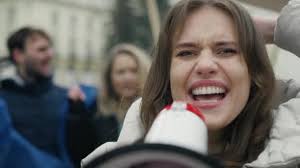 Mujer caucásica mirando a la cámara y gritando a través del megáfono frente  a un grupo manifiesto de jóvenes. Fotografía con cámara de helio RED en 8K.  556356898