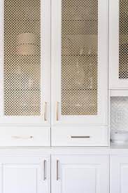 A pink, orange, and purple abstract art piece hangs over a pink tray placed atop a white bar cabinet finished with white mesh doors and gold knobs. Gold Metal Kitchen Cabinet Door Panels Transitional Kitchen
