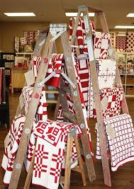 A Creative Idea Use Ladders To Display Tablecloths Dishtowels And Table Runners In Your Store Quilt Display Quilt Stores Red And White Quilts