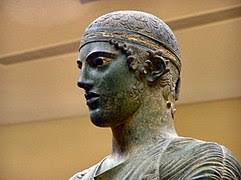 Το άγαλμα του ηνίοχου αποτελεί το σωζόμενο τμήμα χάλκινου συμπλέγματος που είχε αφιερωθεί στο ιερό από τους δεινομενίδες, δυναστική οικογένεια της γέλας στη σικελία. Hnioxos Agalma Delfwn Bikipaideia