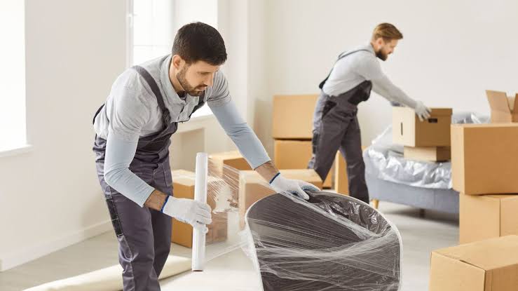 Movers wrapping sofa mattress and fragile furniture before loading
