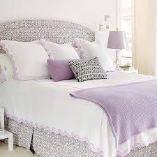 White and lavender bedroom features lavender walls framing a carved wood 4 poster bed dressed in white and lavender bedding flanked by white campaign nightstands with shelves accented with x trim atop gray geometric rug. White And Lavender Scalloped Bedding Design Ideas
