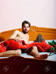 Jovem Bonito Barbudo Homem Macho Atlético Com Barba À Moda Deitado Nu Na  Cama Sob O Cobertor Vermelho Em Torno De Rosas Alaranjadas E Coração  Decorativo Dos Namorados Cinza No Fundo Da