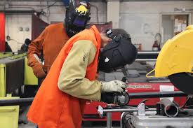 A pipefitter wearing full PPE while welding on an industrial job site.
