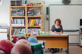 Classroom With Teacher Sitting Behind Her Desk Working On Papers By Paul Phillips
