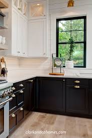 White penny tiles with gray grout create a stunning backsplash design around white cabinets with brass trim. Black Windows And Lower Base Cabinets Accent The Upper White Cabinets And Shipl Kitchen Cabinets Black And White Modern Farmhouse Kitchens Black Lower Cabinets