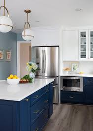 A Navy Blue Center Kitchen Island Is Lit By Gold And White Pendant Lights Topped With A White Quart Navy Kitchen Cabinets Kitchen Remodel Blue Kitchen Cabinets