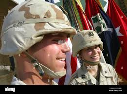 Captains Brandon Holden, left, and his wife Jamie stand in front of a flag  from the 4th Infantry Division , Thursday, Oct. 2, 2003 at their base in  Tikrit, Iraq after they