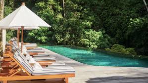 Eight Pool Lounge Chairs With Striped Cushions White Umbrella Lined Up Near Blue Swimming Pool On Sunny Day Luxury Resort Ubud Hotels Ubud