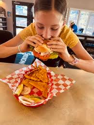 Isla Scharnweber digging into our Cilantro Lime Chicken sandwich!! Look at  that perfect posture!! Elbows out, hunched over the basket!!  #cilantrolimeforpresident2024 Join us for dinner!!!