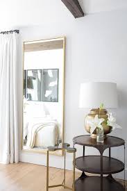 Beside White French Pleated Curtains A Gold Full Length Mirror Is Mounted On A White Wall Next To A G Round Metal Accent Table Metal Accent Table Hammered Lamp