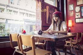 This simple cafe has food that is tasty and a staff that is warm and welcoming; Woman Sitting At Table In Coffee Shop Filtered Carefree Stock Photo 155233330