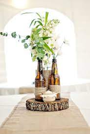 White Floral Filled In Brown Bottles As Rustic Wedding Centerpice Bottle Centerpieces Wine Bottle Centerpieces Diy Table Decor