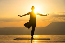 Yogi in tree pose on a wooden deck at sunrise